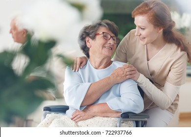 Old lady in glasses sitting in a wheelchair and smiling at her nurse