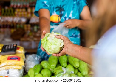 An old lady hands over a piece of white cabbage to a vendor. Buying vegetables at a sari-sari store.