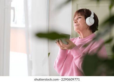 old lady with headphones, enjoying her coffee and music. technology can enhance the quality of life for the elderly by providing access to entertainment and communication. - Shutterstock ID 2290609771