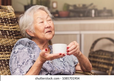 Old Lady (japanese Descendant) Seated Comfortably At Home Holding A Cup Of Tea With A Happy Expression Of Who Is Having A Good Conversation Or Telling Stories.