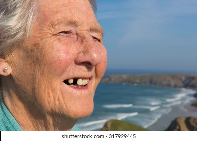 Old Lady Pensioner With Happy Smile But Dental Problems With Her Teeth And A Tooth Missing By Beautiful Coastal Scene