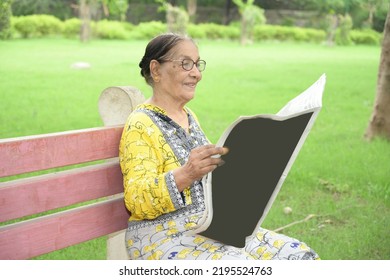 An Old Lady Sitting With Newspaper In Park