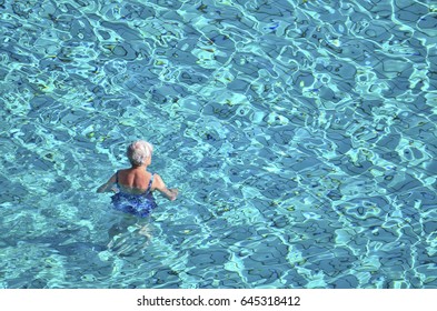 Old Lady Swimming In Clear Swimming Pool.