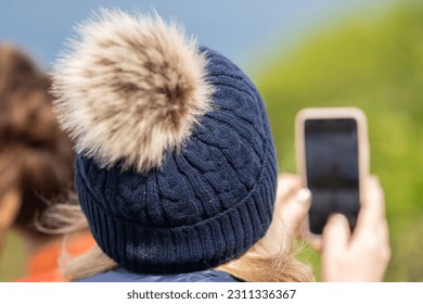 Old lady taking a photo on her phone, wearing a beanie. - Shutterstock ID 2311336367