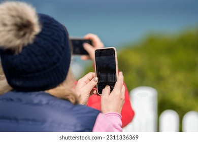 Old lady taking a photo on her phone, wearing a beanie. - Shutterstock ID 2311336369