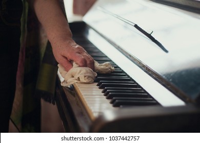 The old lady's hand wiping the dust off the piano keys with a cloth