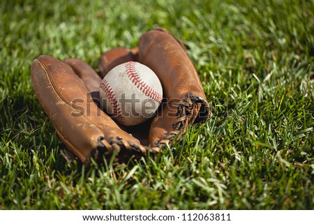 Old leather baseball glove with a ball in the grass