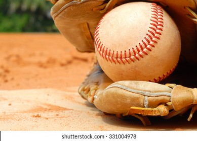 An Old Leather Baseball Mitt, Or Glove With A Worn Baseball Laying On A Home Plate. There Is Clay Around. Home Plate Needs To Be Dusted Off. Bright Sunshine, Horizontal Composition.