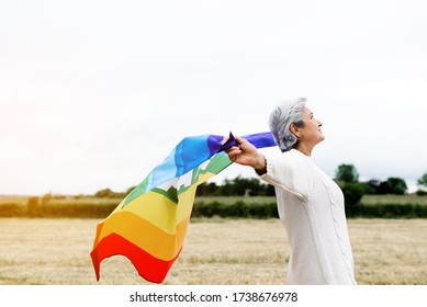 Old Lesbian Woman With Gay Pride Flag In A Field. LGBT Concept And Old Age.