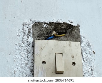 Old light switch mounted on a broken damaged concrete wall showing electrical wires.