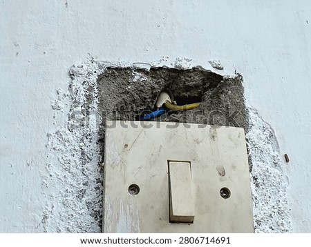 Old light switch mounted on a broken damaged concrete wall showing electrical wires.