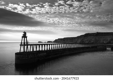 The old lighthouse on the east pier at the harbor of Whitby, North Yorkshire Coast at sunrise with the cliffs on the background.  