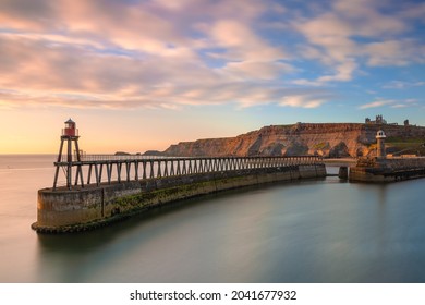The old lighthouse on the east pier at the harbor of Whitby, North Yorkshire Coast at sunrise with the cliffs and the abbey on the background.  