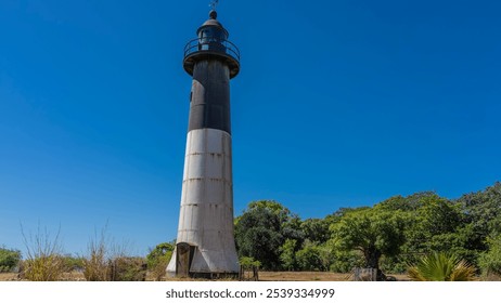 The old lighthouse on the island. A tall black and white tower against a clear blue sky. Lush green vegetation. Madagascar. Faro Nosy Iranja - Powered by Shutterstock