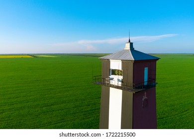 Old lighthouse with red stripes in spring field. Scenic landscape with a tall lighthouse.