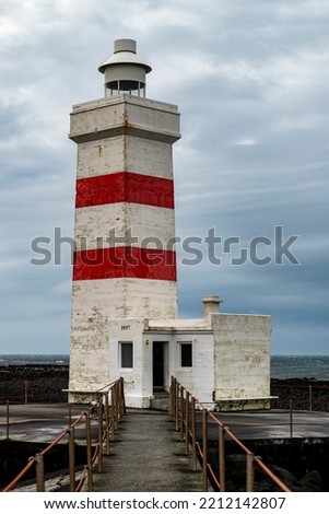 The old Garðskagi lighthouse in Garður under a cloudy sky, Reykjanes Peninsula, Iceland. Built in 1897, the old lighthouse with square ground plan is about 12.5 meters high.