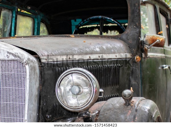 Old, lonely, abandoned car,\
black. The body metal is coated with rust. Round headlight close\
up.