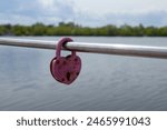 Old love lock in shape of hart on the pipe fence near lake water