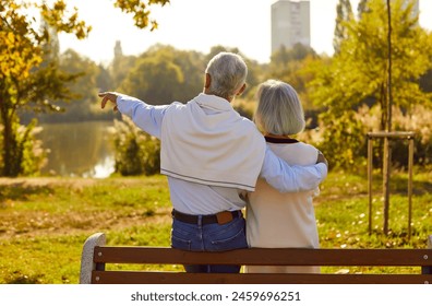 Old love is truest love. Romantic senior couple in love on date talking while sitting on park bench. Back view of mature man hugging his wife and showing her something from distance on warm evening. - Powered by Shutterstock