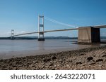 The old M48 Severn bridge from England to Wales. Wide with stony shore in foreground