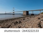 The old M48 Severn bridge from England to Wales. Wide with stony shore in foreground