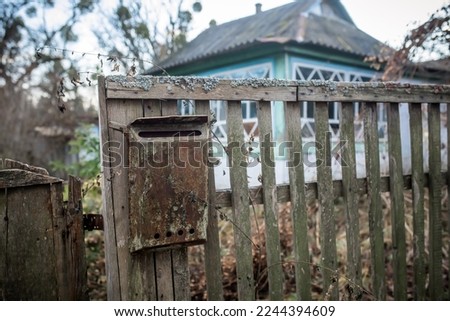 An old mailbox on the fence. Vintage rusty mailbox on a wooden fence near the gate of an abandoned house. The abandoned house of Ukrainians. Life of migrant migrants.