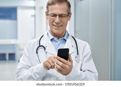 Old Male Doctor Holding Smartphone Using Mobile Phone E Health Technology In Hospital. Modern Tech Medical Healthcare Patients Virtual Consultation App, Telehealth Online, Tele Medicine Appointment.