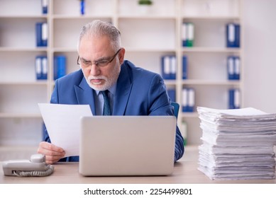 Old male employee and too much work in the office - Shutterstock ID 2254499801