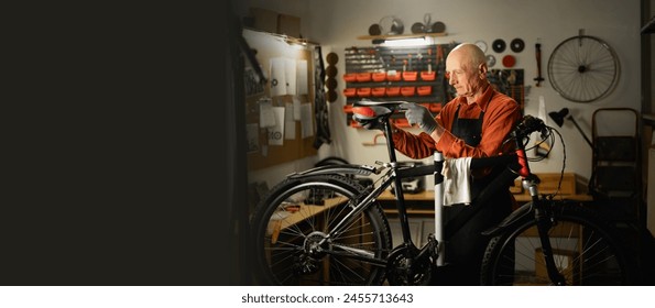 Old male mechanic working in bicycle repair shop, mechanic repairing bike. Copy space. Banner - Powered by Shutterstock