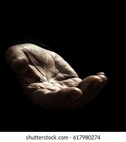 Old Man Asking For Support With Outstretched Hand With Wrinkles On The Black Background. The Concept Of Infirmity And Lack Of Money And Food In The Elderly People Without Sufficient Social Assistance.