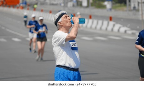 Old man athlete drink water bottle. Thirsty tired senior jog runner. Elder jogger sport work out. 60s sportsman train city street. Thirst person take break. Sprinter stop run marathon. Heavy breath. - Powered by Shutterstock