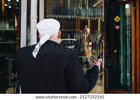 old man behind front windowshop of prayer beads shop