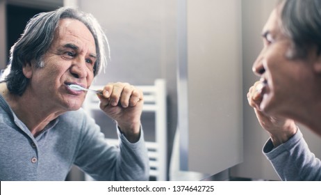 Old Man Brushing Teeth In Front Of The Mirror