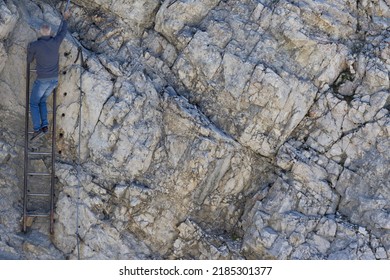 Old Man Climbing Up Ladder On Rock During Summer. Back View.