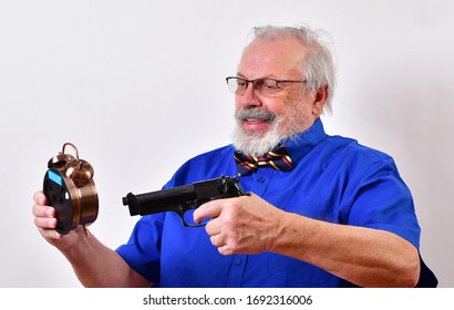 Old Man Dressed In Blue Shirt And Bow Tie Is Really Angry With His Alarm Clock And Threatens To Shoot It.
Crazy Man Points Gun At Alarm Clock.