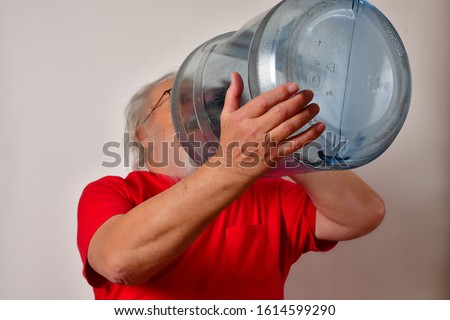 Old man drinking from a 5 gallon water bottle.
Thirsty man drinks from a 5 gallon water bottle.
Thirsty old man drinking from a large bottle.