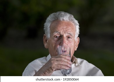 Old Man Drinking Water From Big Glass In Garden