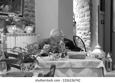 An Old Man Eating Alone In A Tavern Located In Cortona, Tuscany, Italy 15/08/2011. Cortona Is A Medieval Village, Unesco Heritage. Black & White Photo
