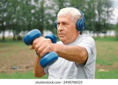 Old man exercising with dumbbells outside. Physical therapy. Elderly 60s male working out. Active sporty gray haired man standing with weights. Older person doing fitness outdoors. People, gym, sport - Powered by Shutterstock