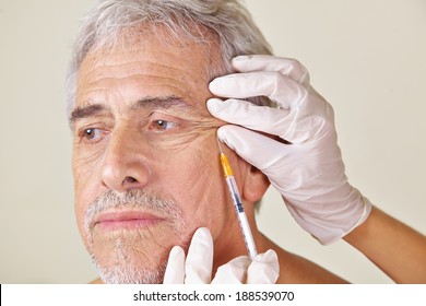 Old man getting wrinkles treatment against crow's feet in beauty clinic