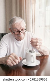 Old Man With Glasses Is Making A Tea Bag. A Man Of 88 Years Old Drinks Tea Sitting At The Table. Old Pensioner Is Happy With Life.