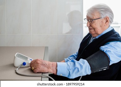 Old Man With Glasses And White Hair Taking His Own Blood Pressure At Home