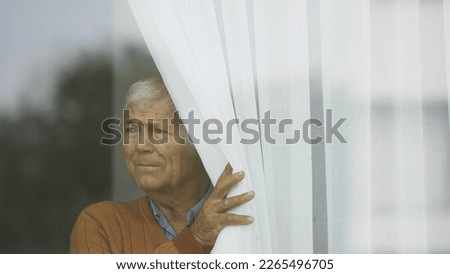 Old man with gray hair inside house put the curtain aside, quarantine, safety