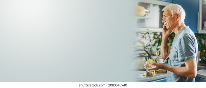 Old Man With Gray Hair And A Mustache, Of The Baby Boomer Generation, Emotionally Gestures. Serious Old Man With Smartphone At Home. Indoors Portrait Of Senior Business Man Using Mobile Phone.