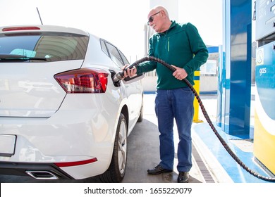 Old man in a green sweater and jeans, filling up with gas in his white ecological car. Filling the tank with compressed natural gas (CNG). Clean energy concept.