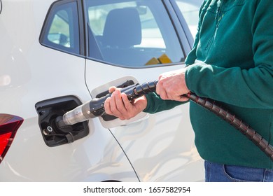 Old man with green sweater and jeans holding the compressed natural gas (CNG) hose to fill the tank of his eco-car. Sustainable energy concept.