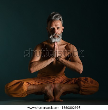 Old man with grey beard doing yoga, pilates, fitness training, stretching exercise, asana or balance workout on floor over blue background. Healthy lifestyle concept