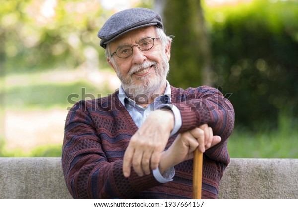 Old man with happy and serene expression sitting\
outdoors on a park bench