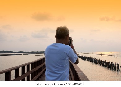 Old Man Holding Camera DSLR Take Photo on Bridge at Sea View on Morning - Powered by Shutterstock