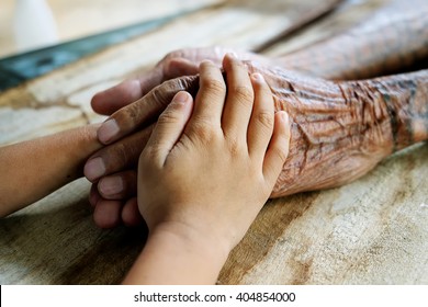 Old Man And A Kid Holding Hands Together On The Wood Table 